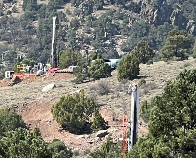 Two core rigs working neighboring pads on a juniper-covered hillside