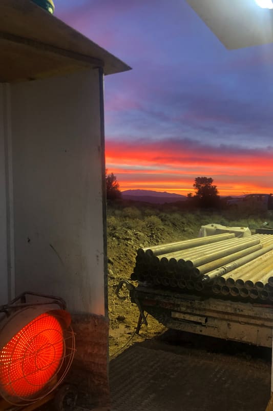 Sunrise over the mountains from the drill shack doorway, heater glowing and a trailer of drill rod in the foreground
