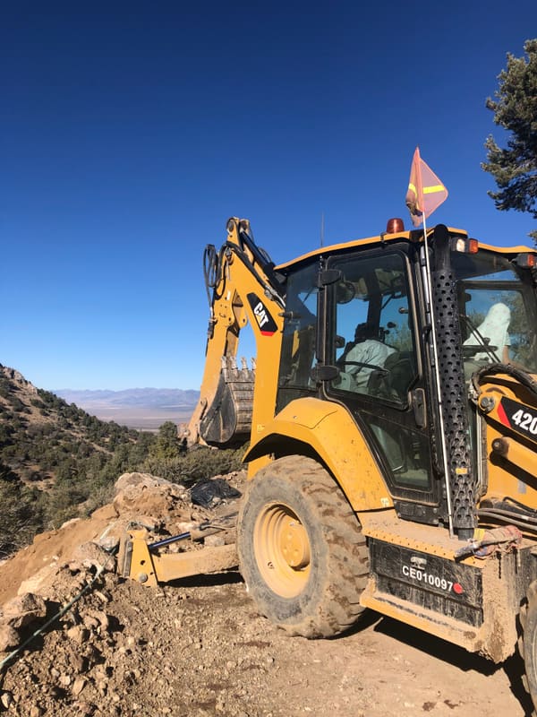 Backhoe regrading a hillside drill pad during reclamation work